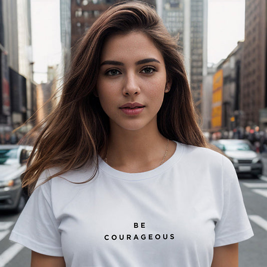 In New York City a young brunette woman wearing a white 100% organic cotton t-shirt that features the positive message, "Be Courageous."