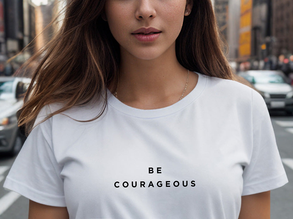 Close-up of a young brunette woman wearing a white 100% organic cotton t-shirt that features the positive message, "Be Courageous."