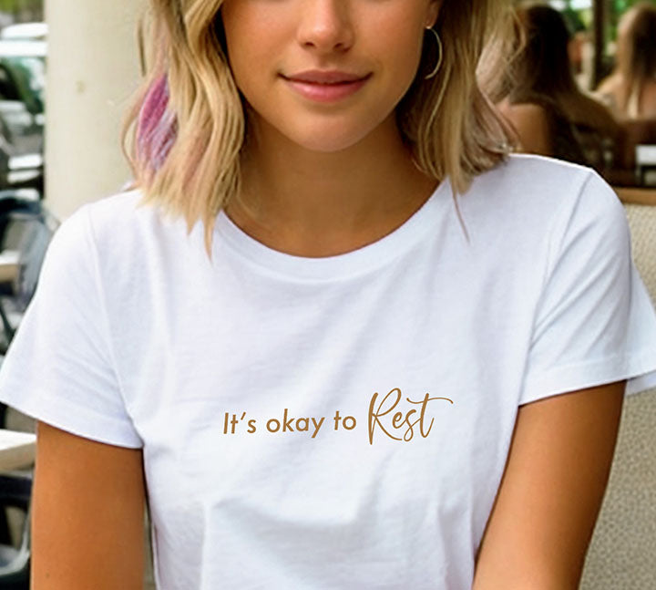 Close-up of a young blonde woman wearing a white 100% organic cotton t-shirt that features the positive quote, "It's okay to REST."