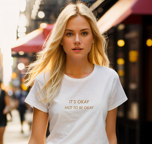 Young blonde woman wearing a white 100% organic cotton t-shirt that features the positive quote, "It's okay to not be okay."