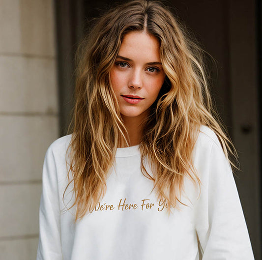 Young blonde woman wearing an oversized organic cotton sweatshirt that features the positive quote, "We're Here For You."